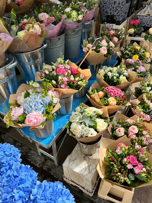 A display of freshly arranged flower bouquets at a flower shop, featuring pink, white, and pastel-colored roses, hydrangeas, and greenery wrapped in brown craft paper and placed in metallic buckets an